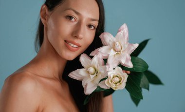 Elinde zambak çiçekleri olan bir portre. Genç kadın stüdyoda arka planda..