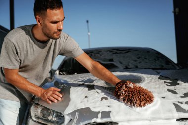 Beyaz temizlik kimyasalı, otomobili yıkamak. Adam dışarıda arabasıyla bekliyor..