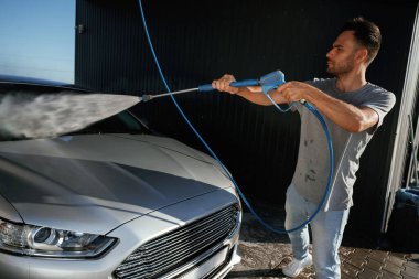 Yan görüş, araba yıkama, yüksek basınç. Adam dışarıda arabasıyla bekliyor..