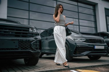 Akıllı telefonlu. Çekici genç bayan dışarıda, yepyeni arabasının yanında..