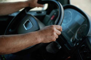 Bir kamyonun direksiyonunu kavrayan ellerin yakın çekimi.