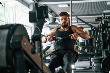 Oturmak, dayanıklılık egzersizi yapmak. Güçlü kaslı adam spor salonunda çalışıyor..