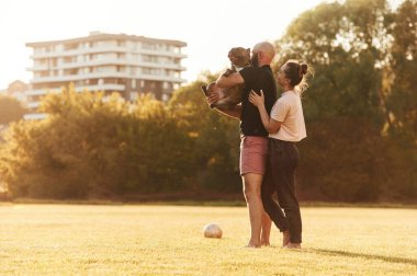 Yan görüş, ayakta duran ve hayvanı tutan. Erkek ve kadın sahada köpekle birlikteler..