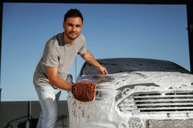 Yüzeyi temizliyor, araba yıkıyor, adam dışarıda arabasıyla bekliyor..