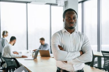 Afro-Amerikalı adam ayakta duruyor. Ofis çalışanlarından oluşan ekip içeride bir arada..