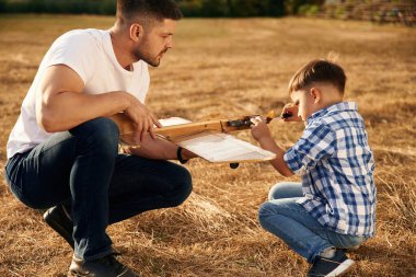 Oyuncağı tamir ederek. Baba ve oğul tahta uçakla sahadalar..