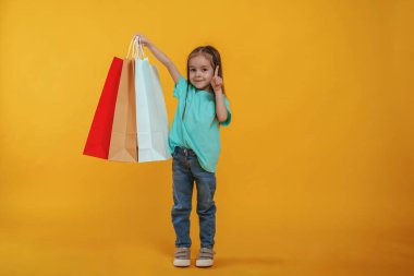 Elde alışveriş torbaları. Sevimli küçük kız sarı arka plana karşı..