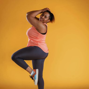 Yan görünüş, poz verme. Tozluklarla. Afrikalı Amerikalı kadın sarı arka planda stüdyoda..