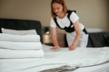 Yatağın üzerinde bir sürü yeni bez var. Genç oda hizmetçisi otel odasında..