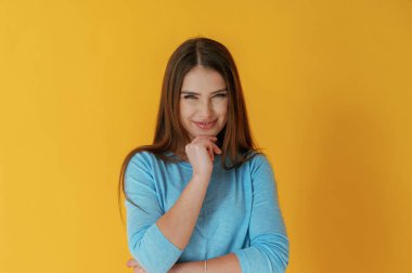 Kötü düşünceler, sevinç gülümsemesi. Genç bayan sarı arka plana karşı..