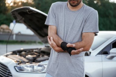 Elde ağrı, kaza, bozuk otomobil. Adam dışarıda arabasıyla bekliyor..