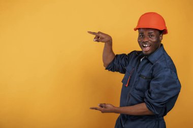 Başlıklı adam fotokopi alanını parmaklarıyla gösteriyor. Yakışıklı siyah adam sarı arka plana karşı stüdyoda..