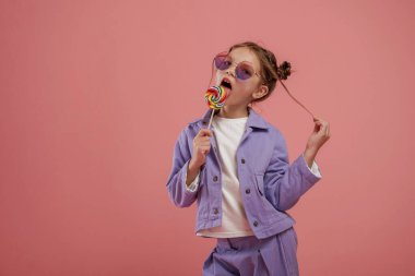 Lezzetli şeker. Şirin küçük kız pembe arka plana karşı..