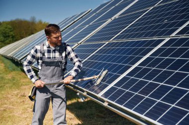 Elleri paspasla. Yüzeyi temizler. Gündüz vakti fotovoltaik güneş panelleri olan bir mühendis..