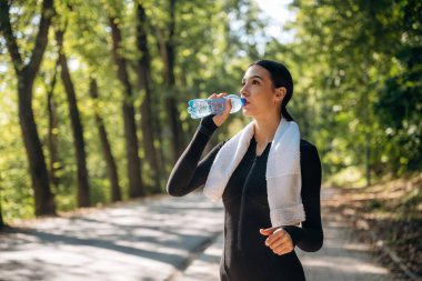 İçme suyu. Genç, sıska kadın dışarıda siyah spor kıyafetleri giyiyor..