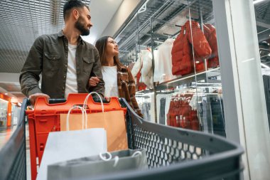 Kıyafetlerin çoğu kenarda. Genç çift süpermarkette beraberler..