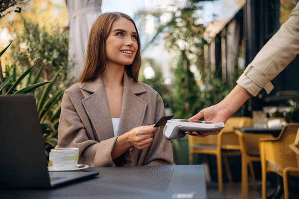 Positive, cheerful facial expression. Woman is paying for food in cafe by using credit card. Conception of wireless money transfer.
