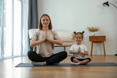 Sakin, nilüfer pozisyonunda. Küçük kızı olan genç bir kadın evde yoga yapıyor..