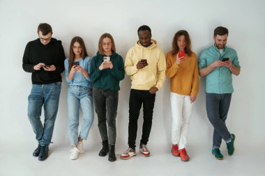 Akıllı telefon kullanmakla meşgul. Bir grup genç beyaz arka planda duruyor..