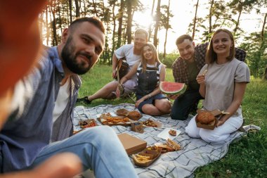 Selfie çekmek, oturmak. Bir grup arkadaş, ekolojik kutularda yiyeceklerle sahada piknik yapıyorlar..