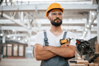 Elinde kablosuz çarpma sürücüsü var. Ahşap depoda sanayi işçisi..