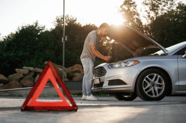 Güneş ışığı altında, kırmızı tabela, kaza, bozuk otomobil, tamir. Adam dışarıda arabasıyla bekliyor..