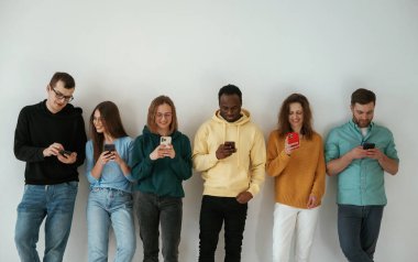 Neşeli, elinde akıllı telefonlar. Bir grup genç beyaz arka planda duruyor..