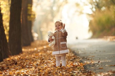 Beyaz oyuncak ayıcık ellerinde. Tatlı küçük kız sonbahar ormanında dökülen yapraklarla..