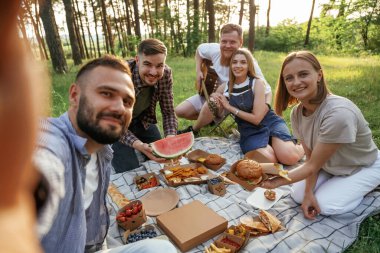 Selfie çekmek, oturmak. Bir grup arkadaş, ekolojik kutularda yiyeceklerle sahada piknik yapıyorlar..