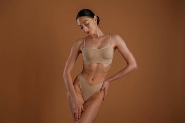 Krem renkli iç çamaşırı. İnce vücutlu kadın arka planda poz veriyor..