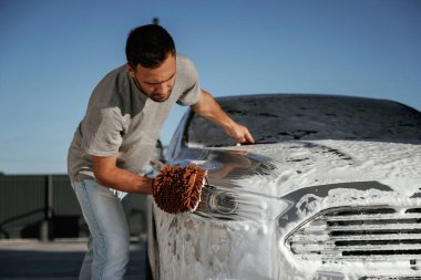 Yüzeyi temizliyor, araba yıkıyor, adam dışarıda arabasıyla bekliyor..