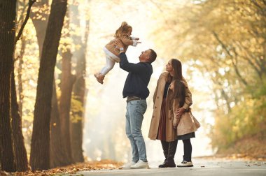 Kızı elinde tutuyor. Mutlu anne, baba ve iki kız çocuk ailesi sonbahar parkında, ormanda, yolda.