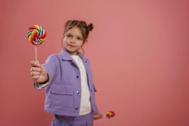 Manzarayı şekerle kapatın. Şirin küçük kız pembe arka plana karşı..