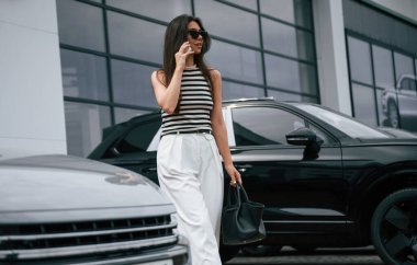 Telefonla konuşuyorum. Çekici genç bayan dışarıda, yepyeni arabasının yanında..