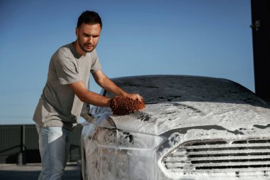 Yüzeyi temizliyor, araba yıkıyor, adam dışarıda arabasıyla bekliyor..