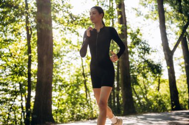 Koşmak, ormanda koşmak. Genç, sıska kadın dışarıda siyah spor kıyafetleri giyiyor..