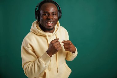 Müzik dinlemek, dans etmek. Afrikalı Amerikalı adam stüdyoda yeşil arka plana karşı duruyor..