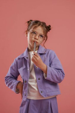 Düşünüyor, kalem tutuyor, zeki öğrenci. Şirin küçük kız pembe arka plana karşı..