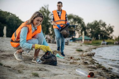 Kıyıda. Bir gönüllü çamurlu bir sahilde çöp topluyor..