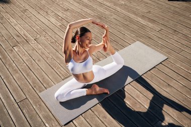 Güneş ışığıyla aydınlatılıyor, yoga yapıyor. Spor elbiseli genç bayan dışarıda..