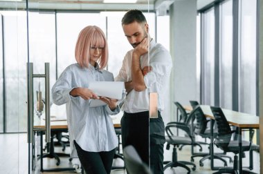 Ayakta duruyorum ve belgeyi okuyorum. Kadın ve erkek ofiste birlikte çalışıyorlar..