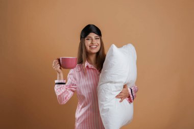 Bir bardak içkiyle, pijamayla ve yastıkla. Genç ve güzel bir bayan stüdyoda arka plana karşı..