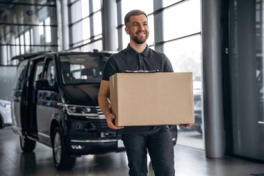 Bir kutuyla, gülümsüyor. Teslimatçı ya da yükleyici arabanın yanında..