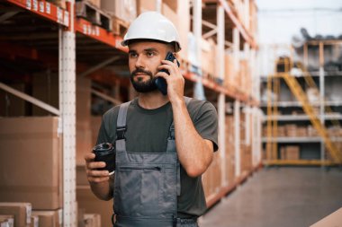 Kahve fincanı ve akıllı telefon ellerinde. Foreman depoda, kargo dağıtım işinde..
