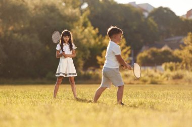 Raketler ellerinde, badminton oynuyorlar. Mutlu çocuklar yaz tarlasında.