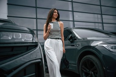 Bir fincan kahve tutuyorum. Çekici genç bayan dışarıda, yepyeni arabasının yanında..