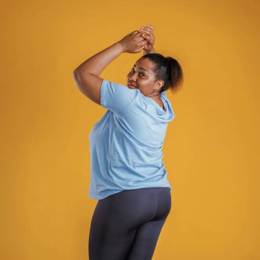 Mavi gömlekli ve siyah spor taytlı. Afrikalı Amerikalı kadın sarı arka planda stüdyoda..