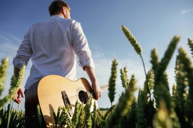 Müzisyen akustik gitarlı. Beyaz gömlekli adam tarlada..