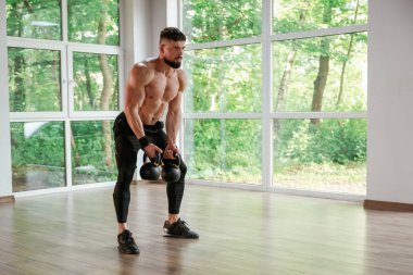 Kalkıyor, dambılları tutuyor. Güçlü kaslı adam spor salonunda çalışıyor..