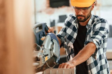 Tahtayı kesmek için testereyi kullanmak. Depoda sanayi işçisi.